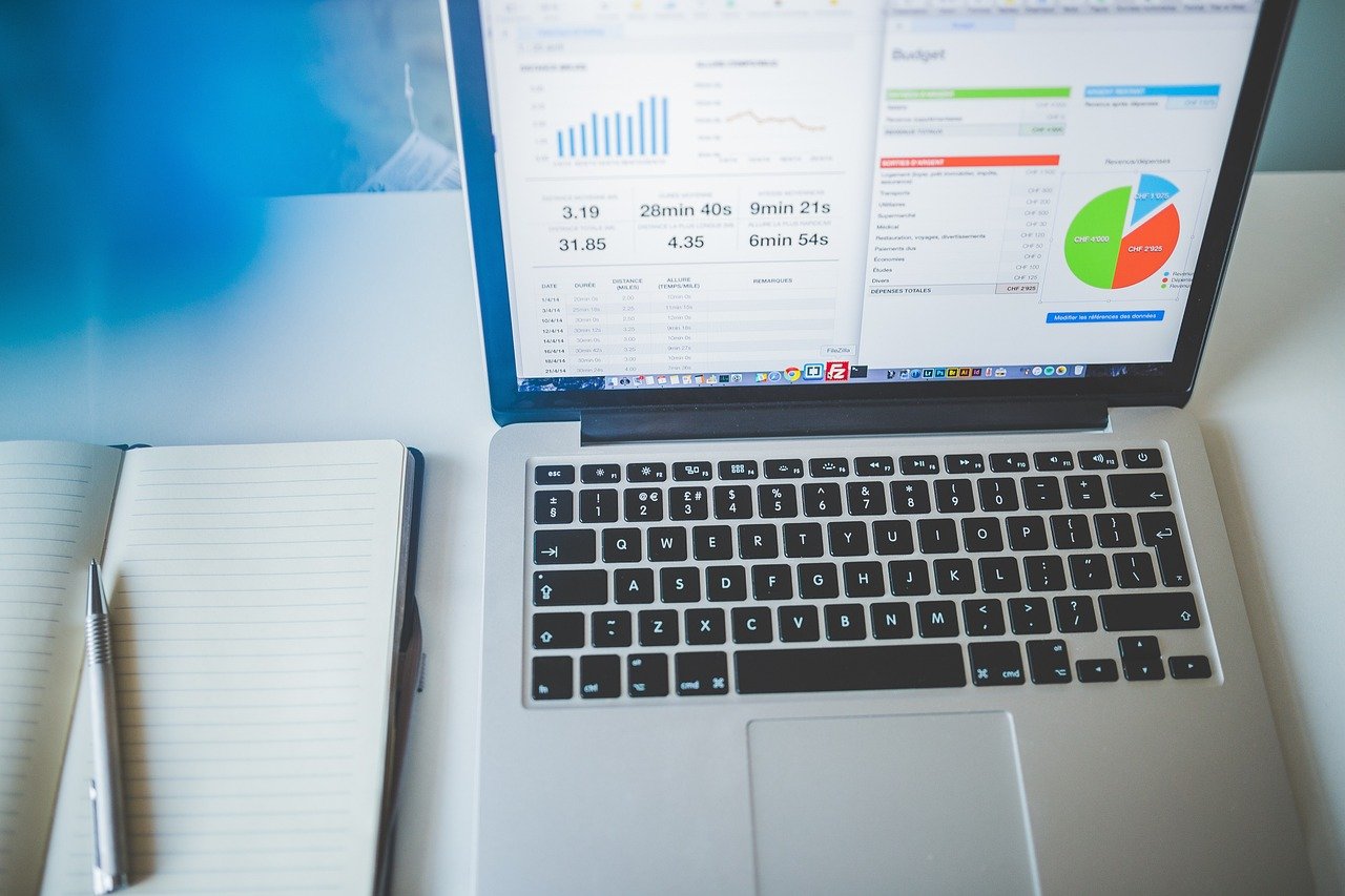 A laptop on a desk showing charts and campaign figures beside an open notebook