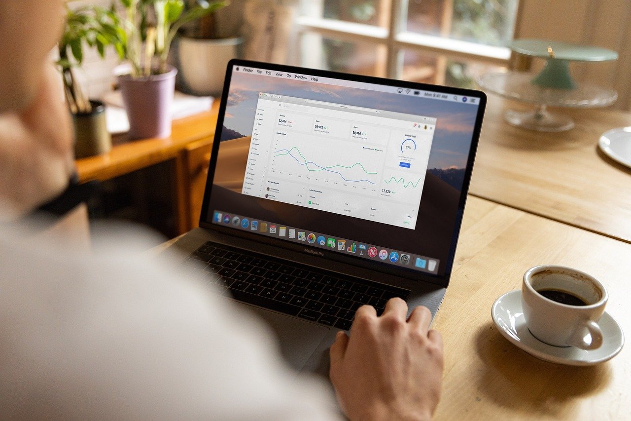A man checking a performance dashboard on his laptop next to a cup of coffee